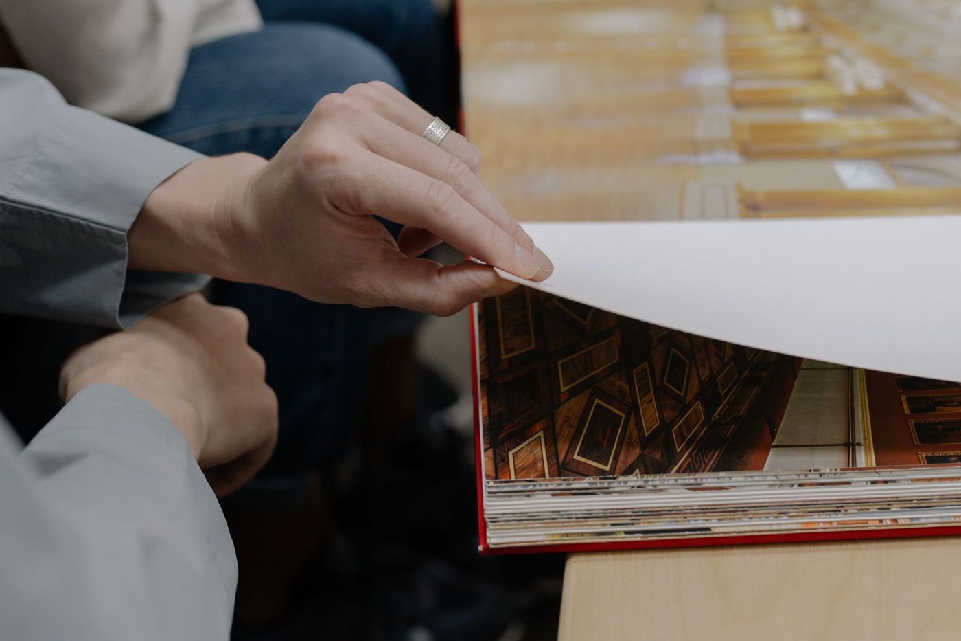 Handen slaan een wit vel om in een groot, rood gebonden fotoboek dat op een houten tafel ligt