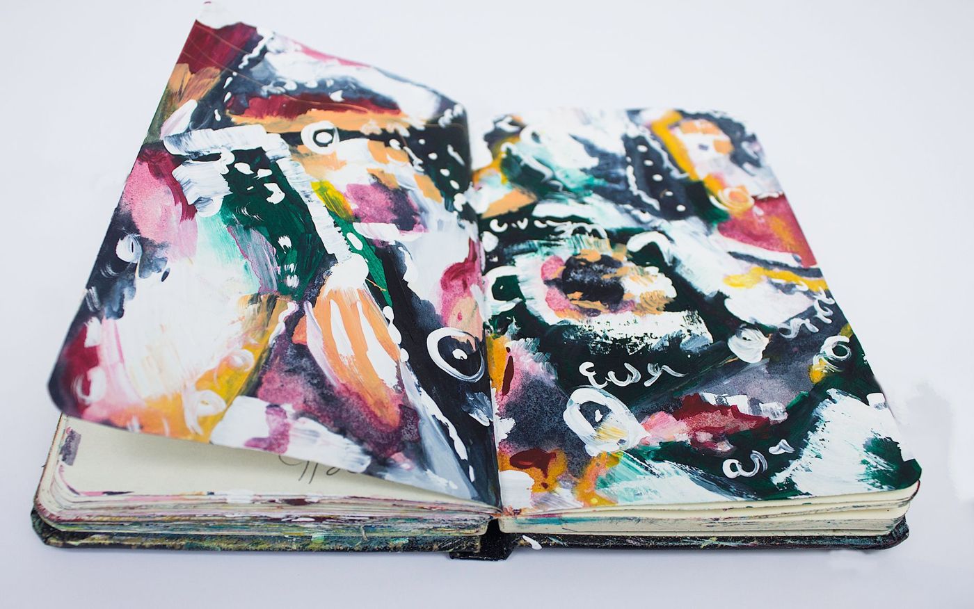Opengeslagen schetsboek met felle abstracte verfpagina's in roze, groen, oranje en zwart met witte krullen en stippen