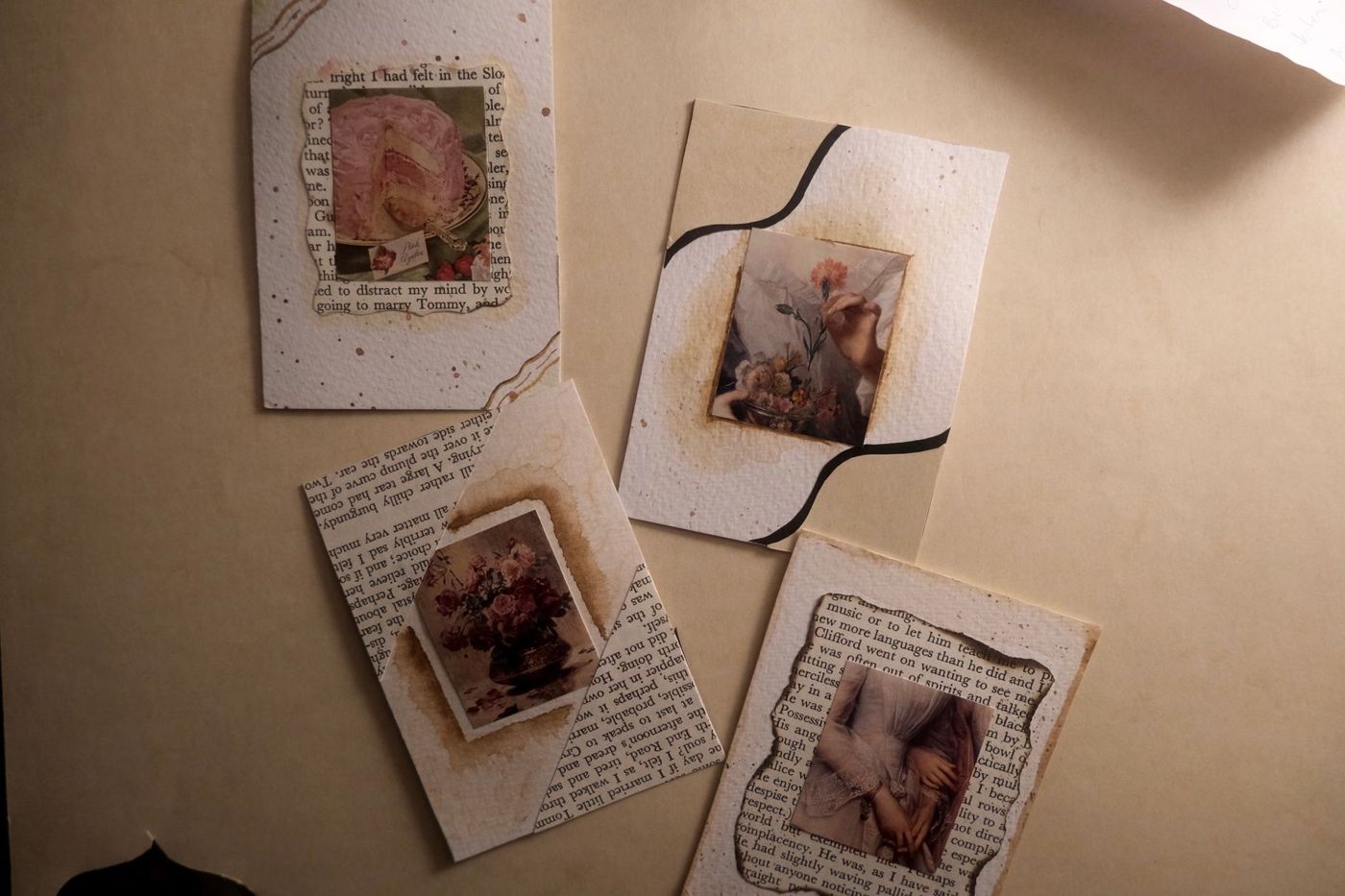 Vier handgemaakte kaartjes met vintage plaatjes van een taart, bloemen en handen op boekpagina's en aquarelpapier