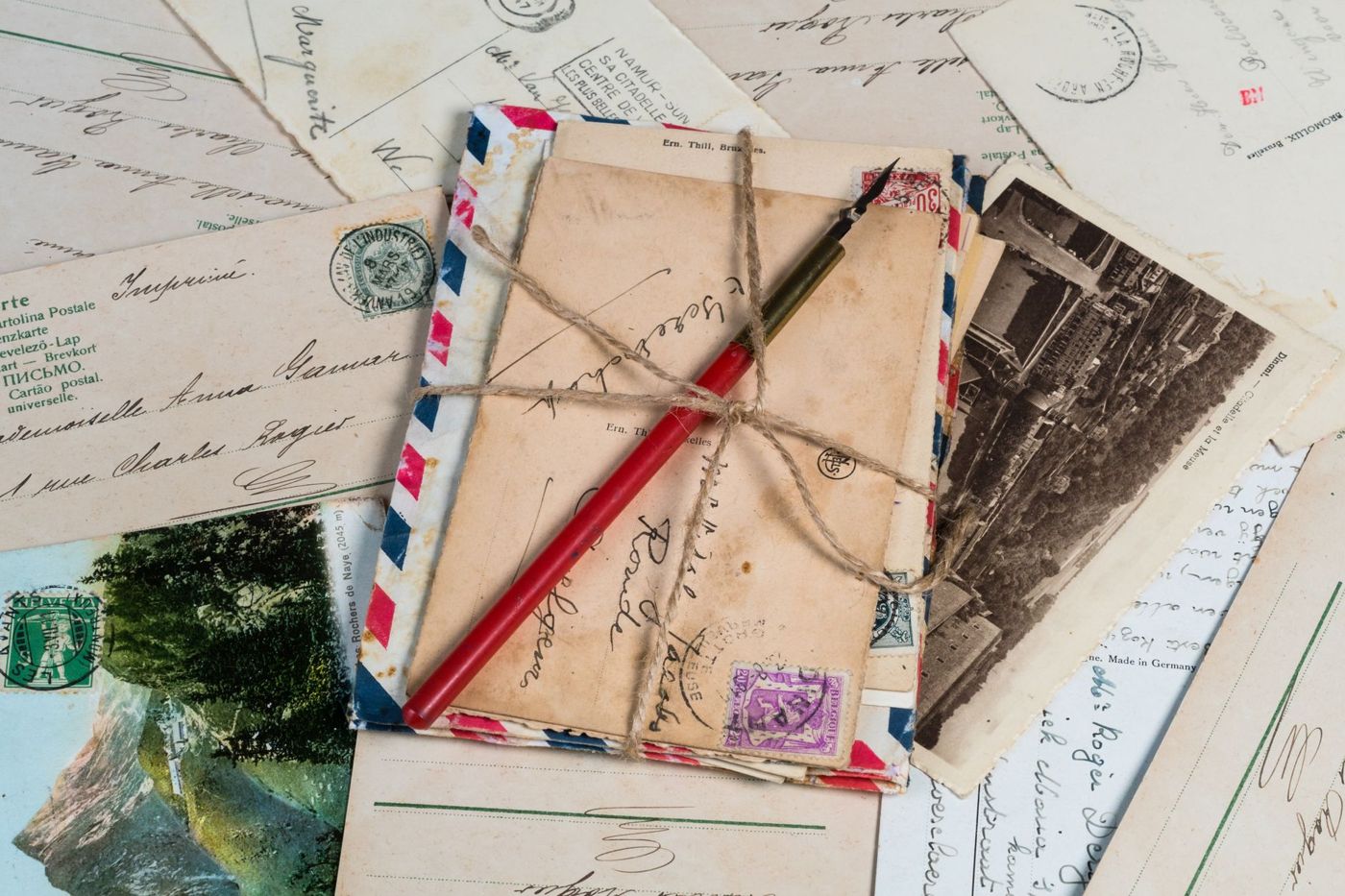 Stapel oude ansichtkaarten en luchtpostenveloppen met touw en een rode kroontjespen, tussen kaarten met handschrift