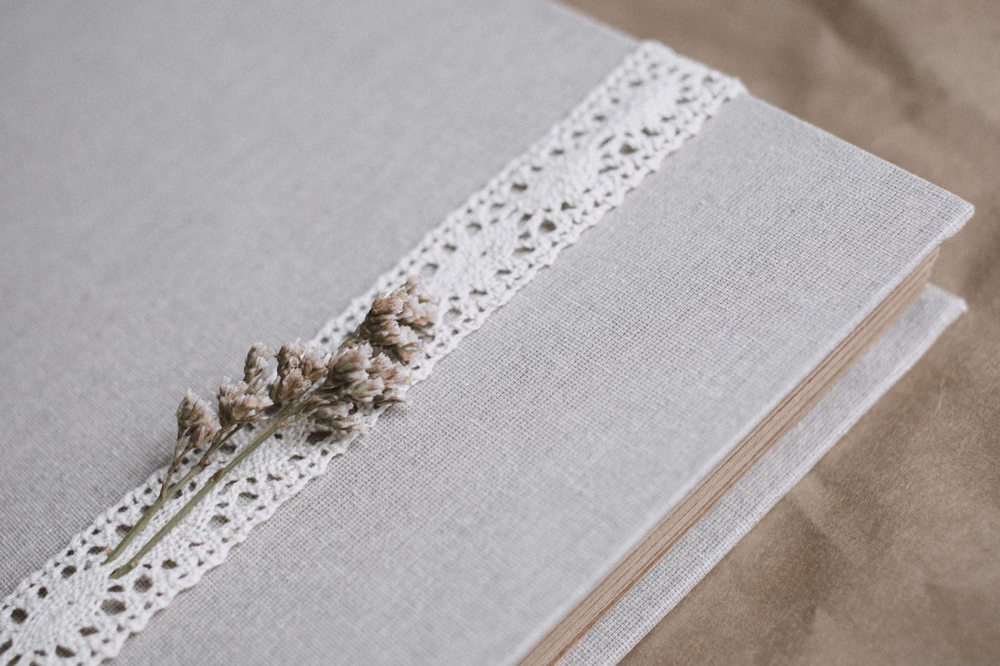 Grijze linnen albumkaft met een strook witte kant en een takje gedroogde bloemen op bruin pakpapier