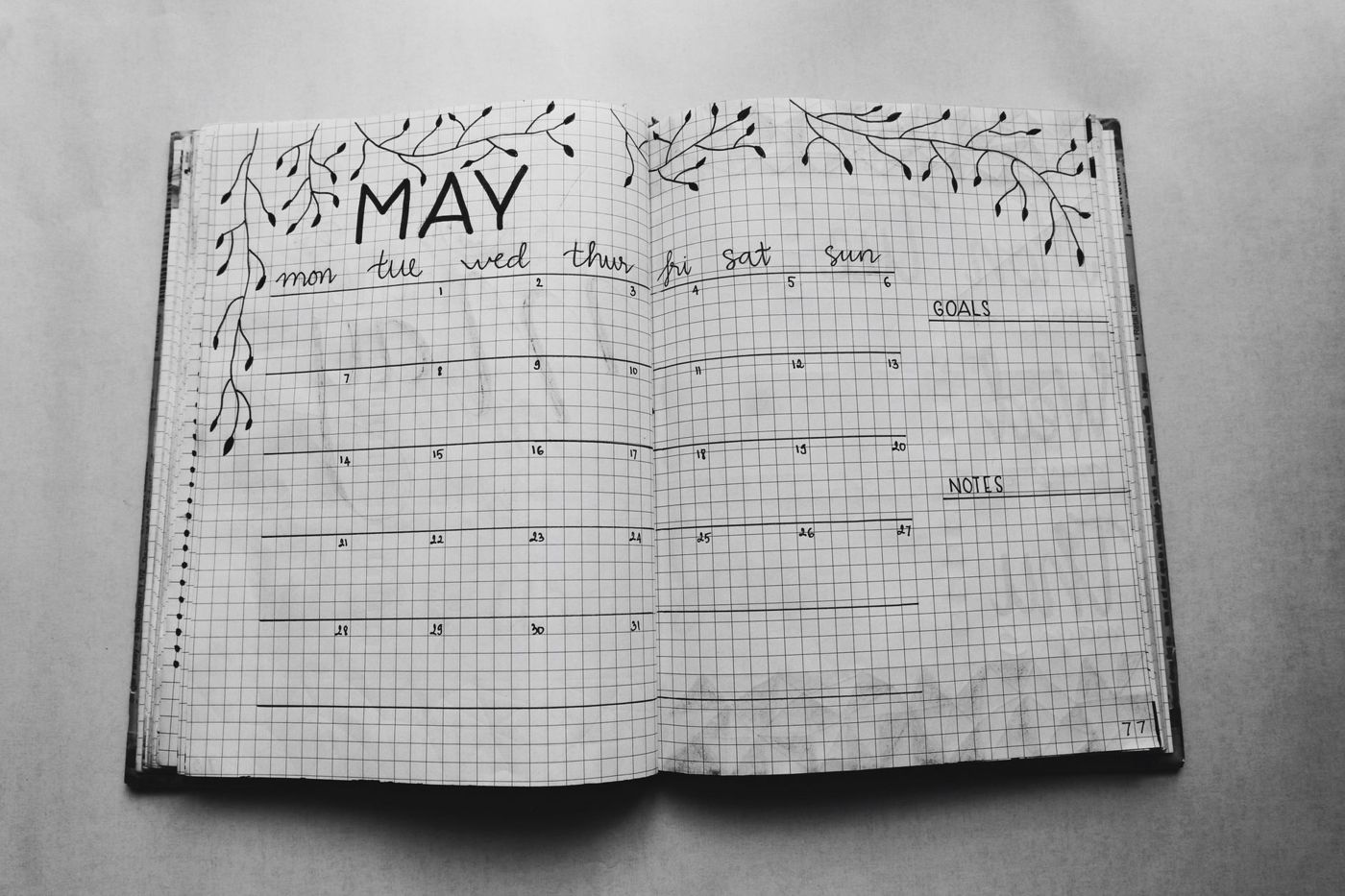 Opengeslagen bullet journal met een maandoverzicht van mei op ruitjespapier, versierd met getekende takjes, in zwart-wit