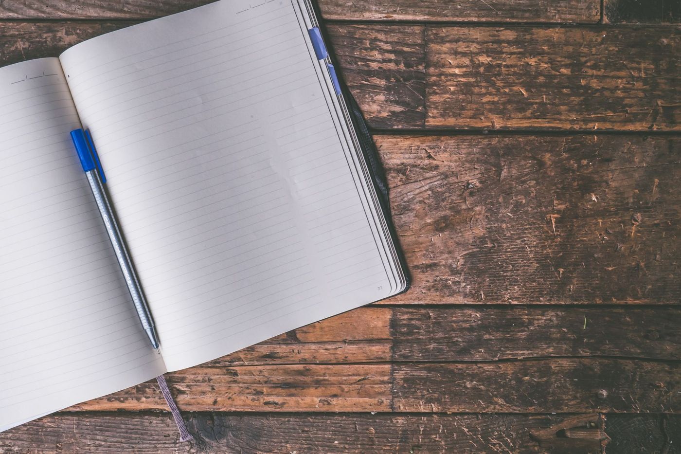 Opengeslagen notitieboek met lege lijntjespagina's en een blauwe pen op een ruwe houten tafel