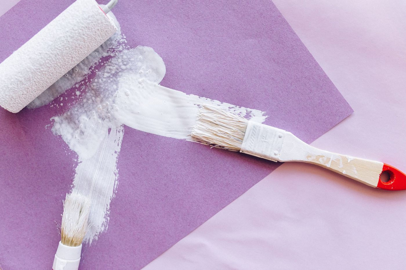 Kwast en roller brengen witte lijmlaag aan op paars papier