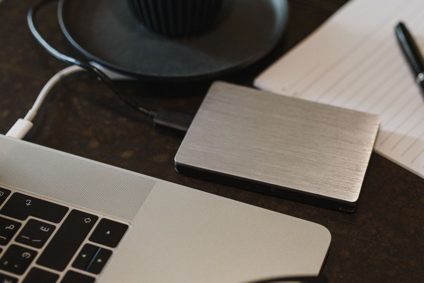 Externe harde schijf van geborsteld metaal naast een laptop en een notitieblok, aangesloten met een usb-kabel