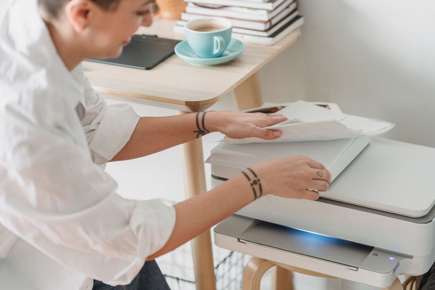 Iemand pakt afgedrukte vellen uit een printer op een houten bureautje