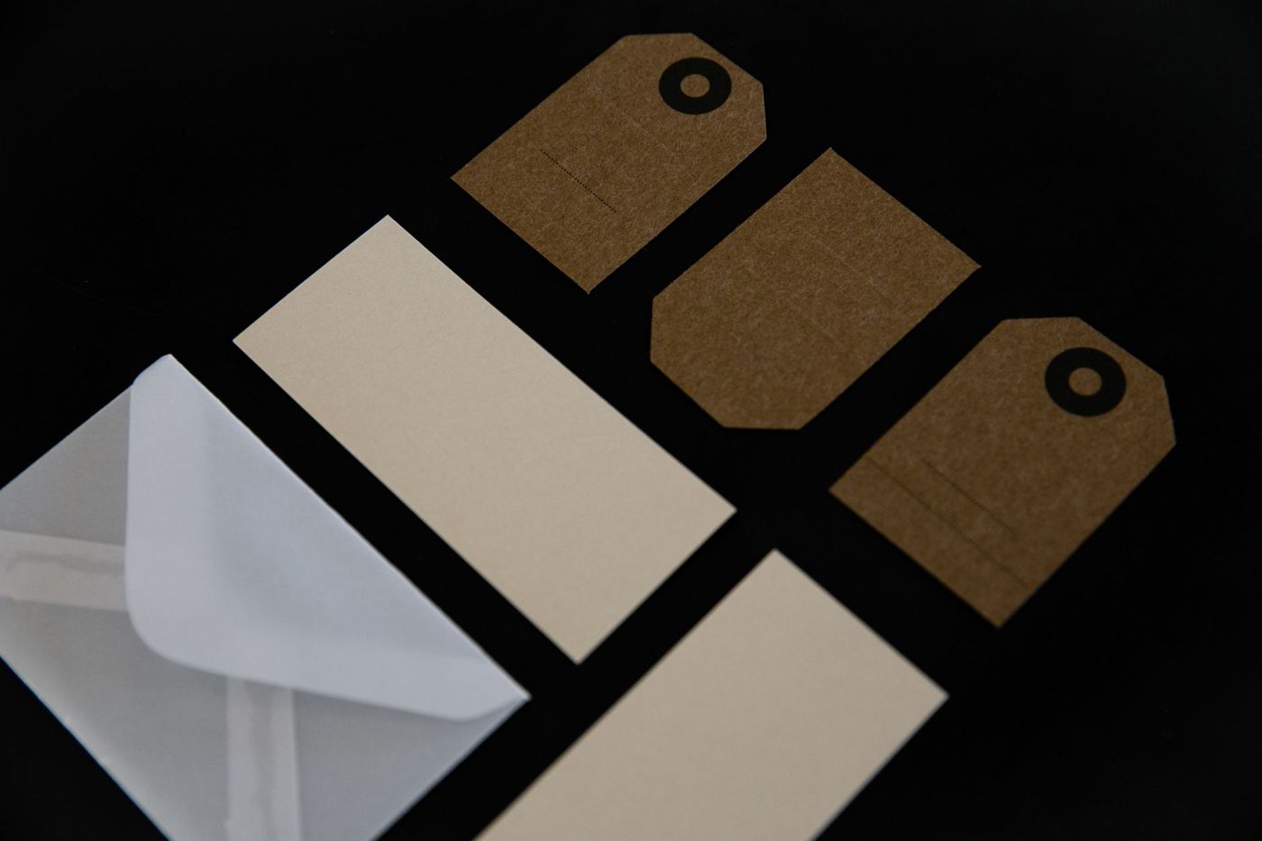 Enveloppen, kraftpapieren tags en crèmekleurige kaartjes naast elkaar op een zwarte ondergrond