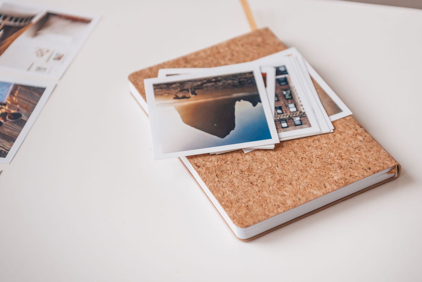 Een stapeltje afdrukken met witte rand op een notitieboek met kurk omslag, op een wit bureau
