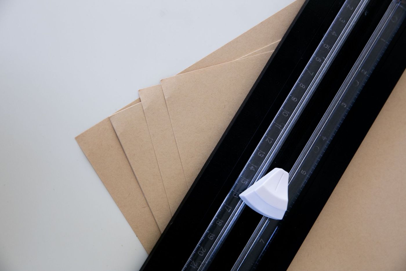 Vier vellen kraftpapier naast een papiersnijder met liniaal op een witte tafel