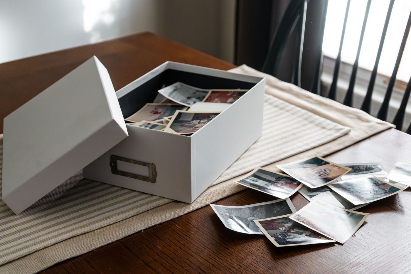 Een open witte fotodoos vol oude kleurenafdrukken op een houten tafel, met losse foto's ernaast
