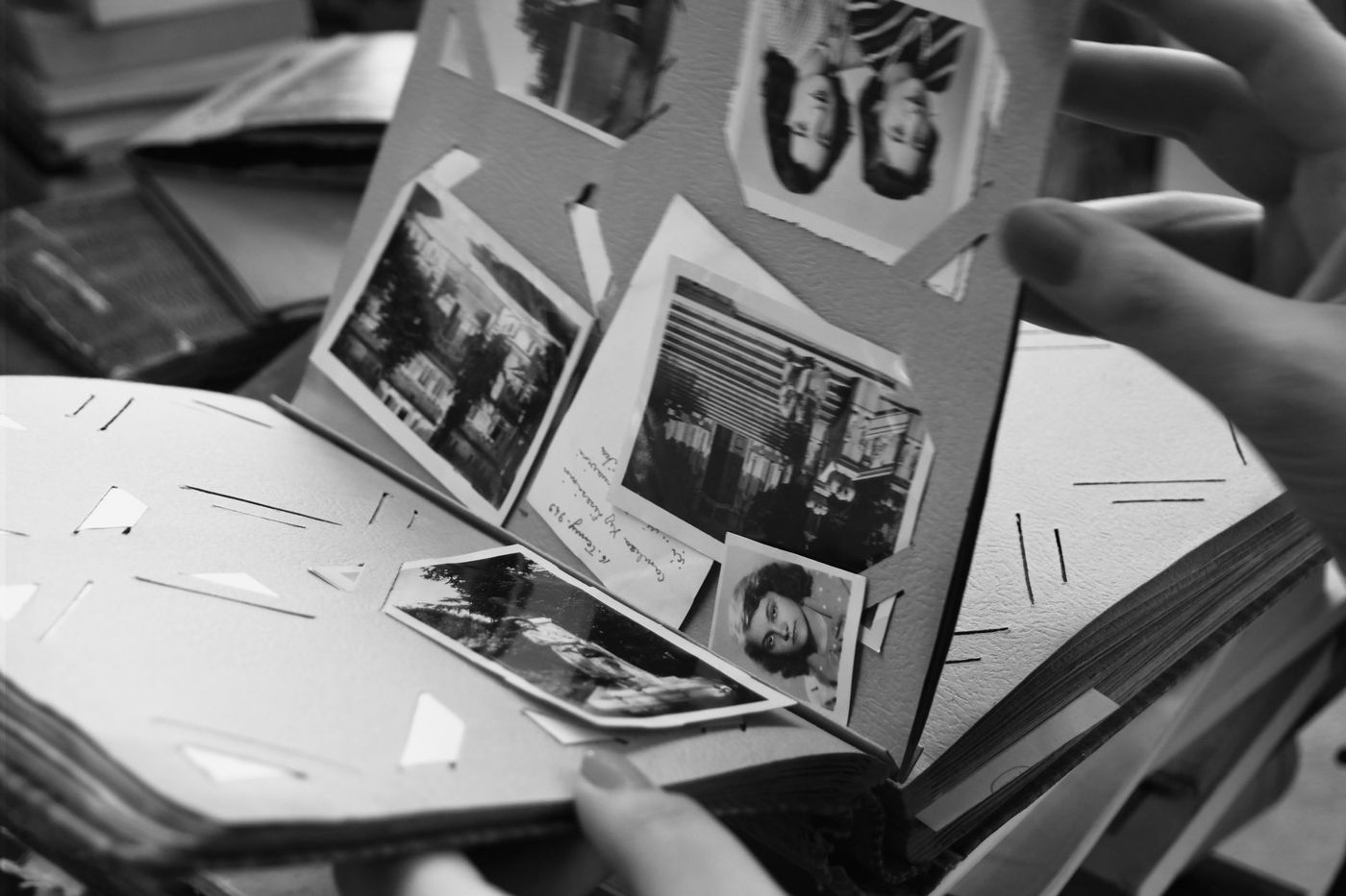 Handen bladeren door een oud zwart-wit fotoalbum met opgeplakte foto's en een handgeschreven notitie