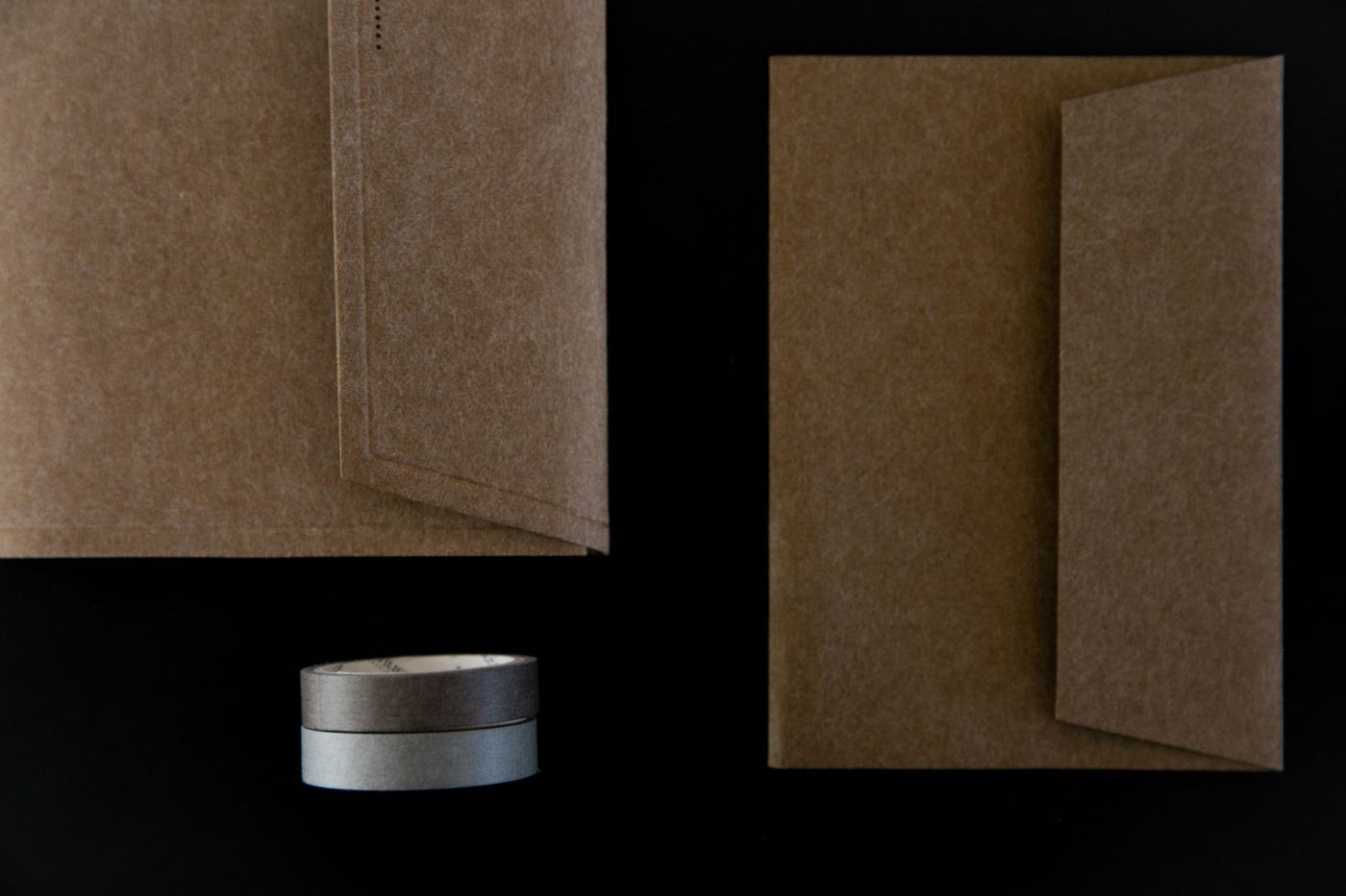 Twee bruine papieren enveloppen en twee rolletjes washi tape op een zwarte ondergrond