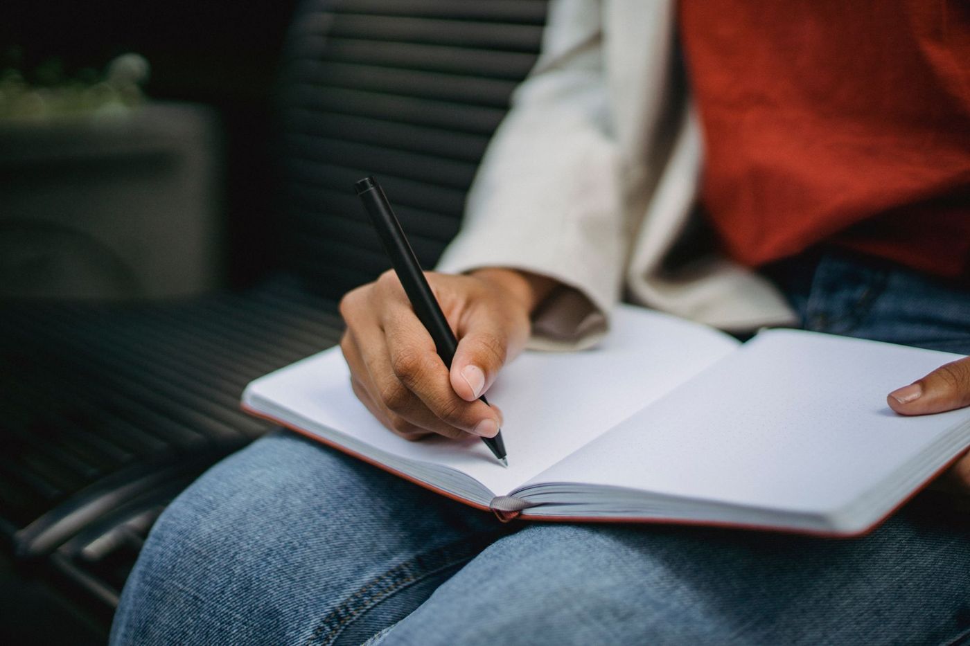 Een hand schrijft met een zwarte pen in een opengeslagen notitieboek op iemands schoot