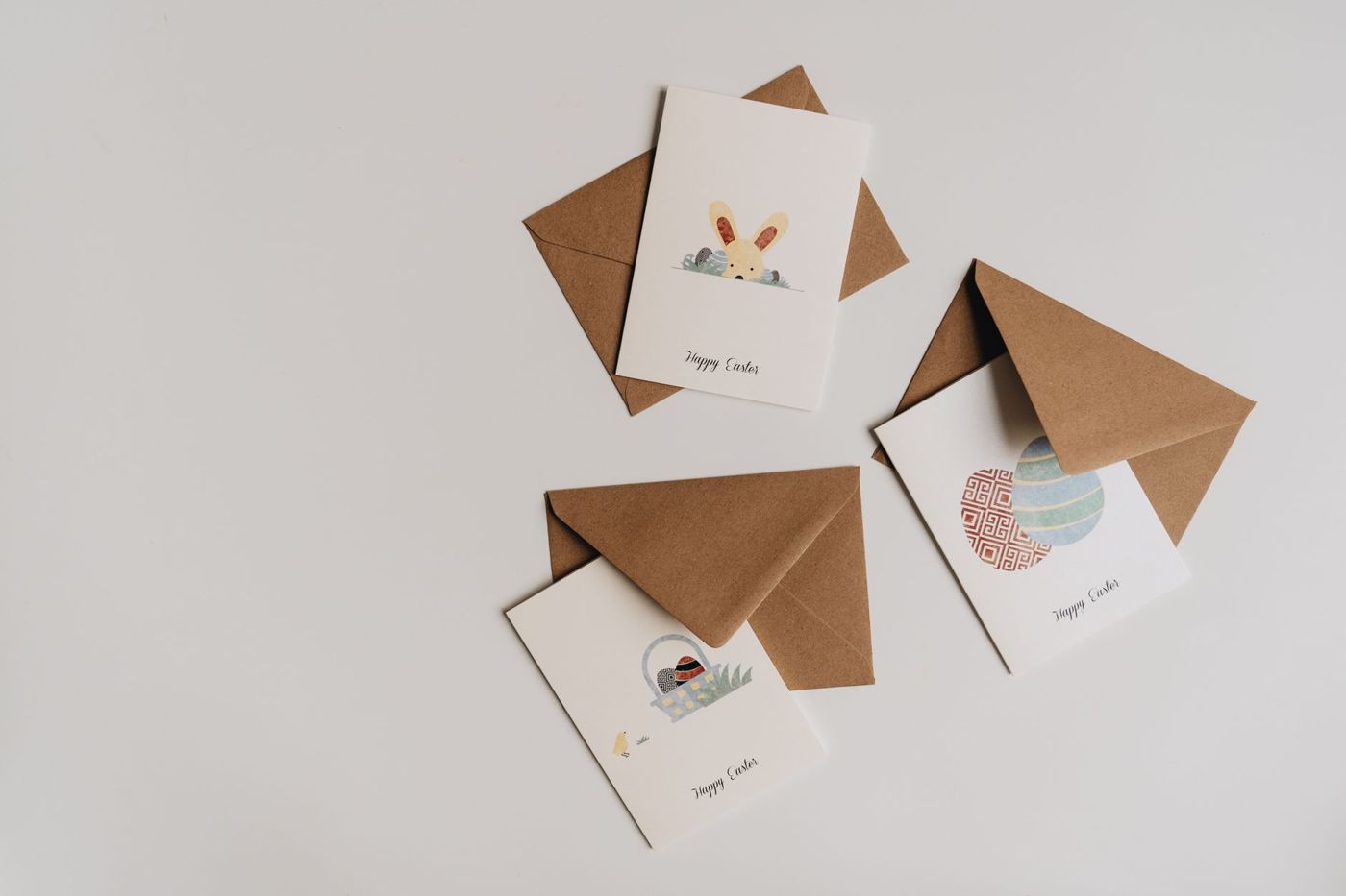Drie witte paaskaarten met een haas, een mandje en eieren, met bruine kraftenveloppen