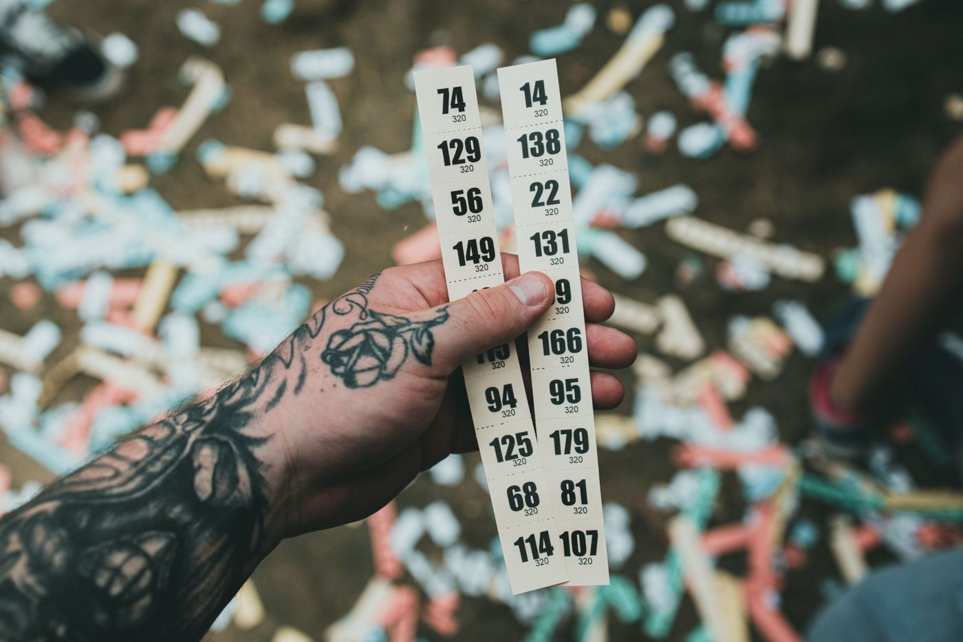 Een getatoeëerde hand houdt twee stroken genummerde kaartjes vast boven confetti op de grond