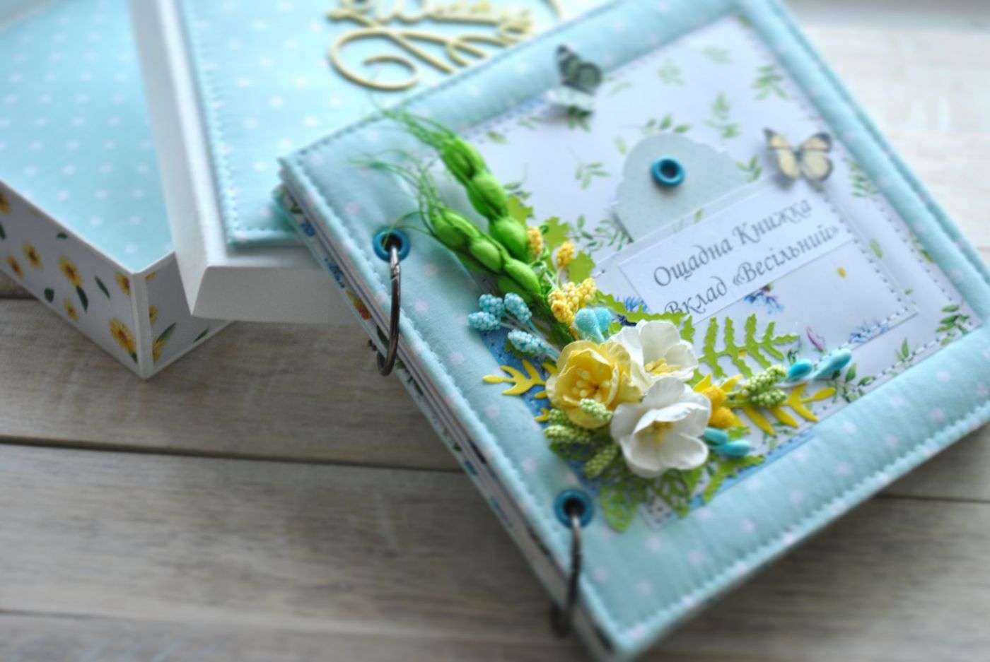 Handgemaakt album in lichtblauwe stof met witte stippen, ringen en op de kaft een boeket van papieren bloemen en vlinders