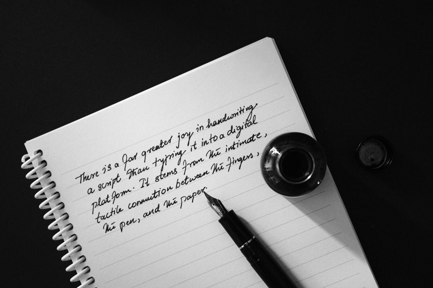 Zwart-witfoto van een spiraalnotitieboek met handschrift in vulpeninkt, met een vulpen en een inktpotje erbij
