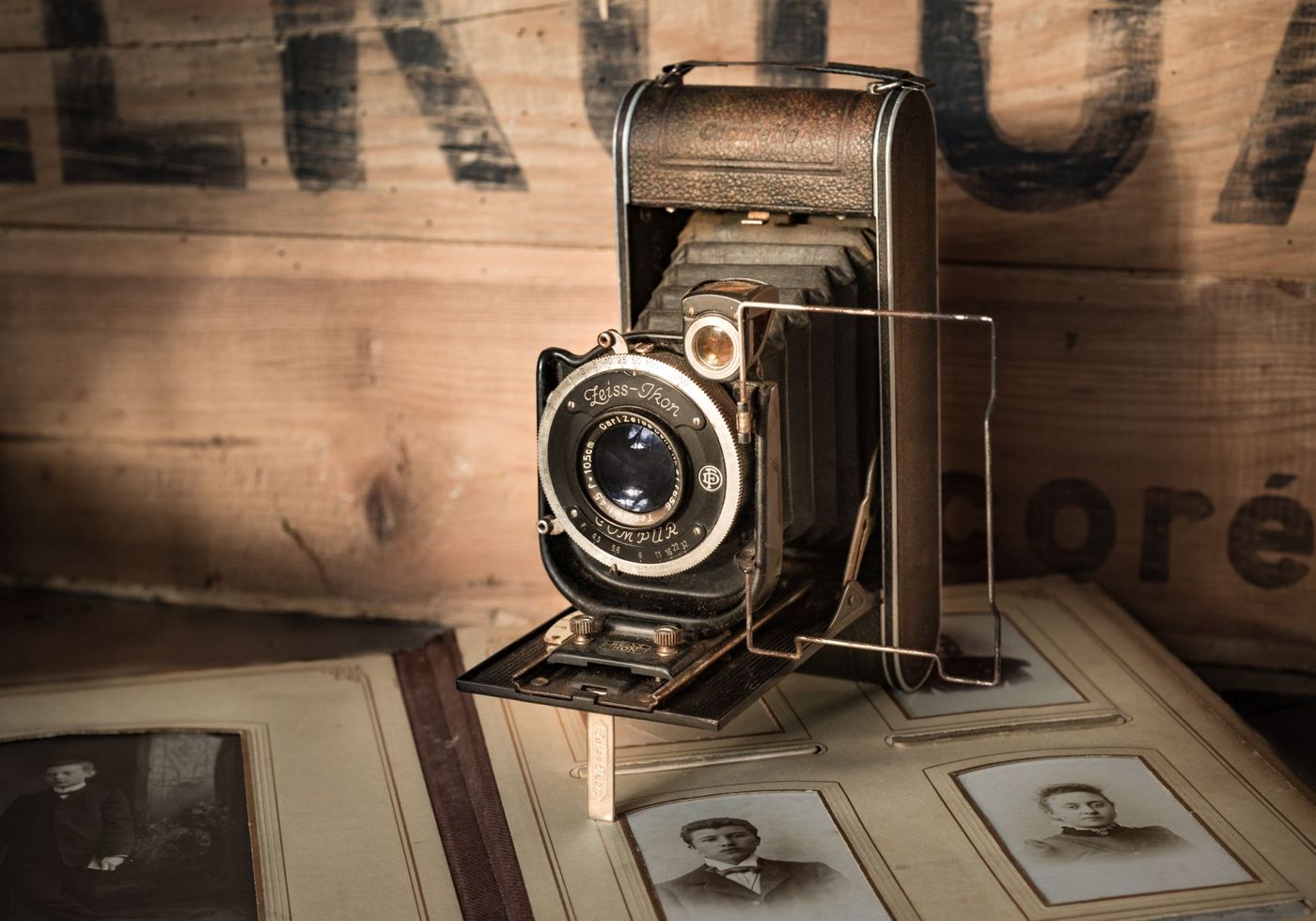 Oude Zeiss Ikon-vouwcamera op een opengeslagen fotoalbum met sepiaportretten op karton, tegen een houten kist