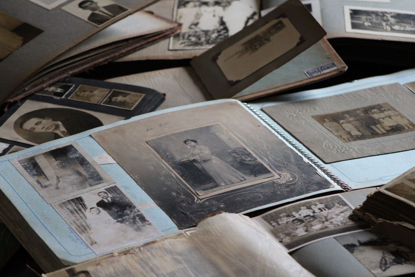 Verspreide oude fotoalbums met zwart-witportretten, in het midden een opengeslagen album met blauwe bladen
