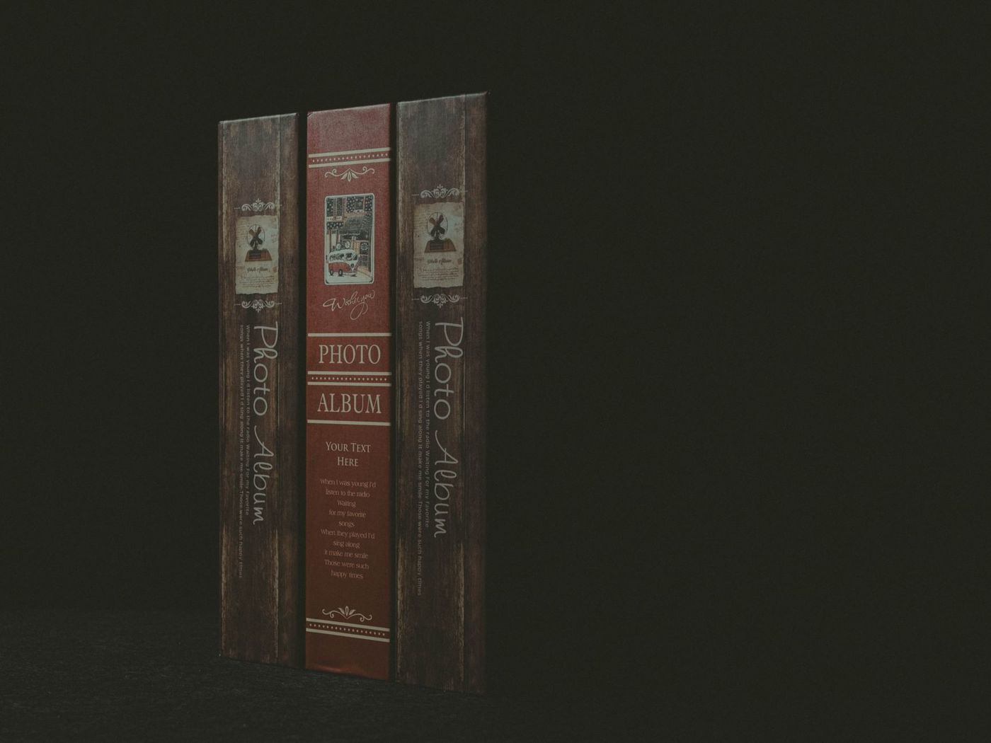 Drie smalle albumruggen met de opdruk Photo Album, een rode tussen twee houtkleurige, tegen een donkere achtergrond