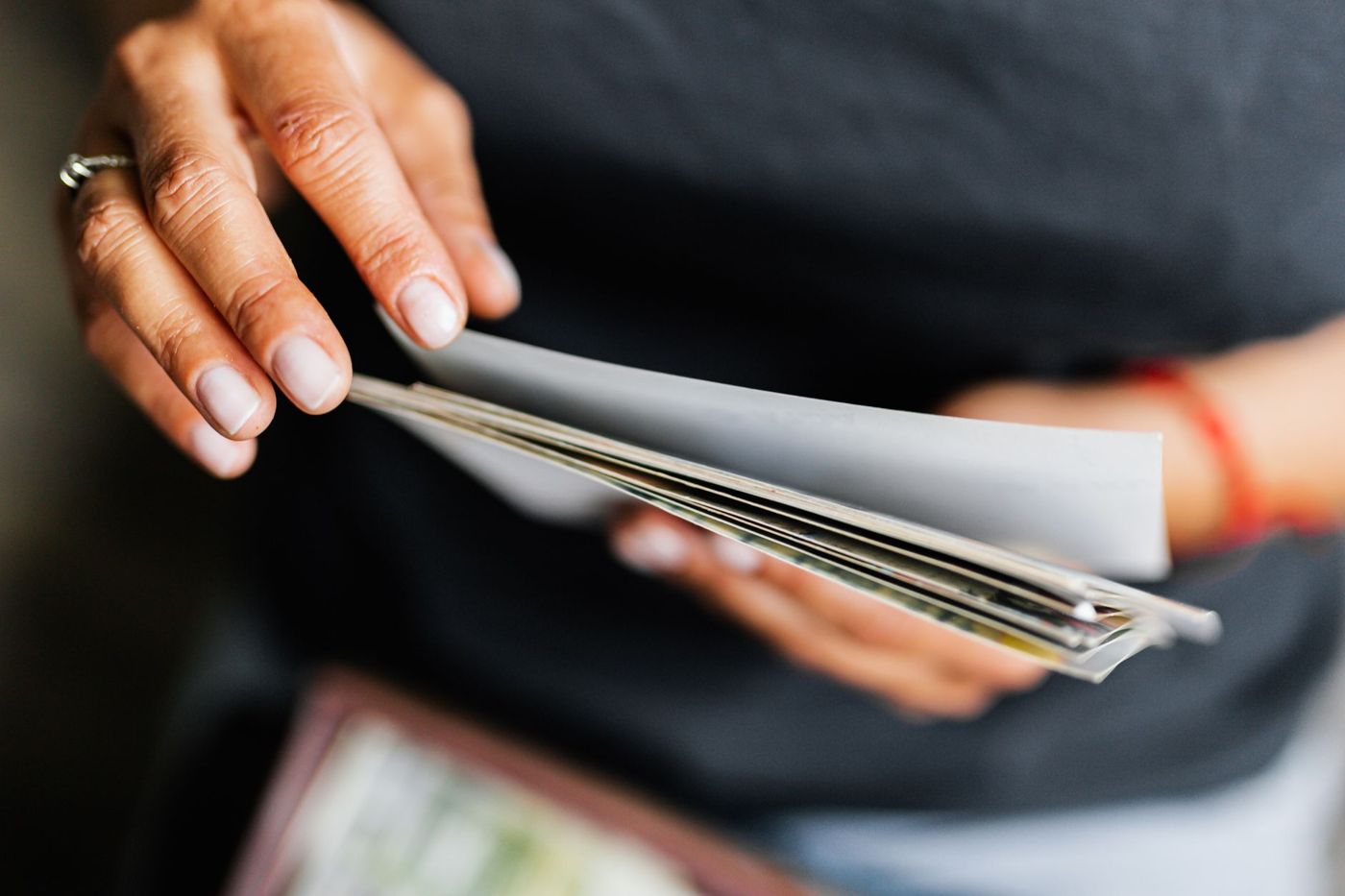 Twee handen bladeren door een stapeltje papieren en afdrukken, tegen een donkere trui