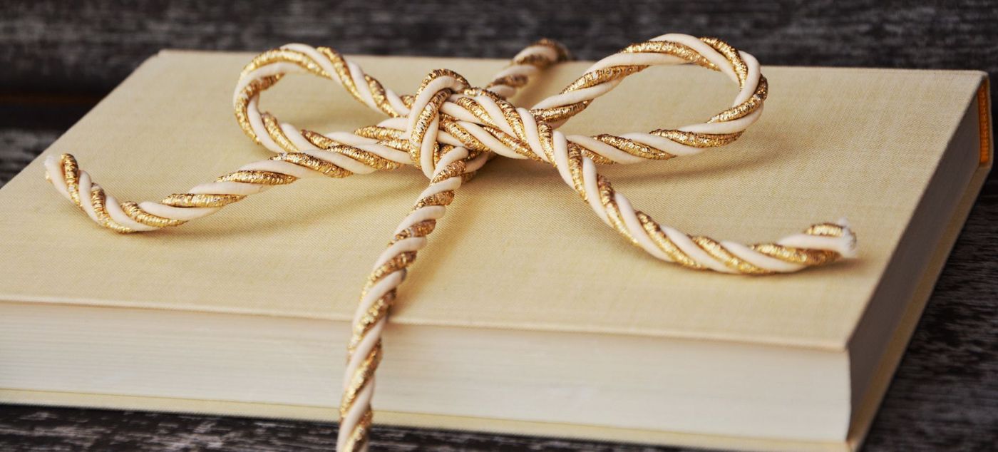 Crèmekleurig gebonden boek met een gedraaid goud-met-crème koord als strik op een grijze houten ondergrond