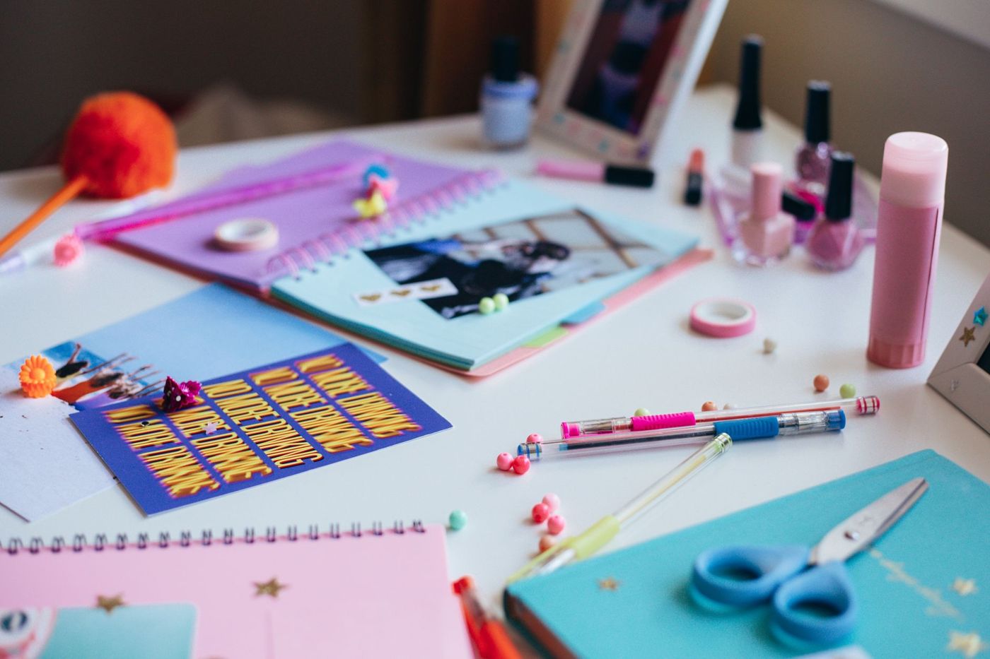 Werktafel met gekleurde schriften, een plakstift, gelpennen, washi-tape en een schaar naast nagellak