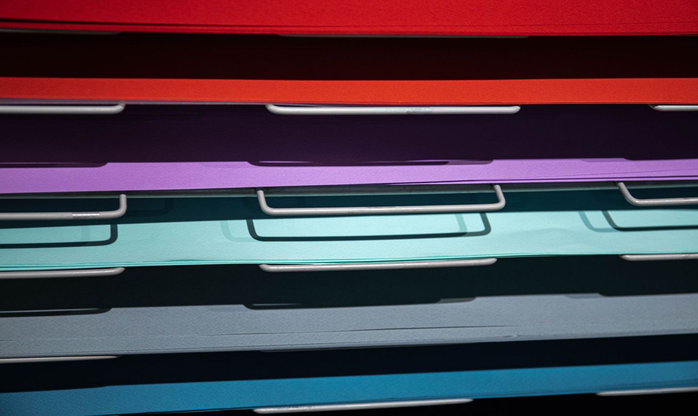 Close-up van gekleurde papierstapels in rood, paars, turquoise en blauw op metalen rekken