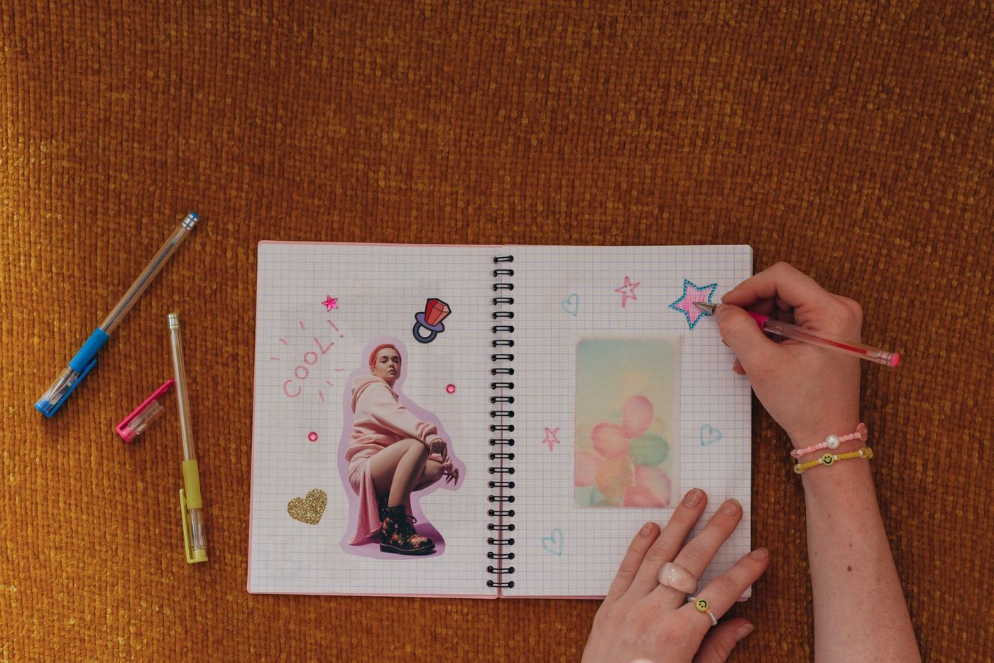 Hand versiert een journalpagina met foto's en stickers op een bruin tafelblad