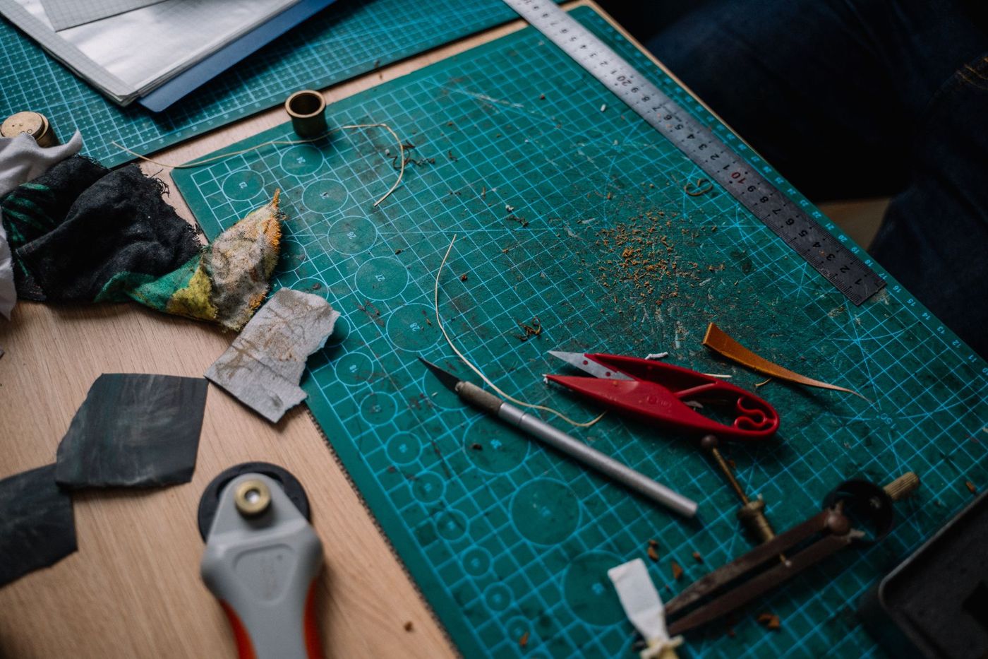 Groene snijmat met metalen liniaal, hobbymes, rode kniptang en een rolmes op een werktafel