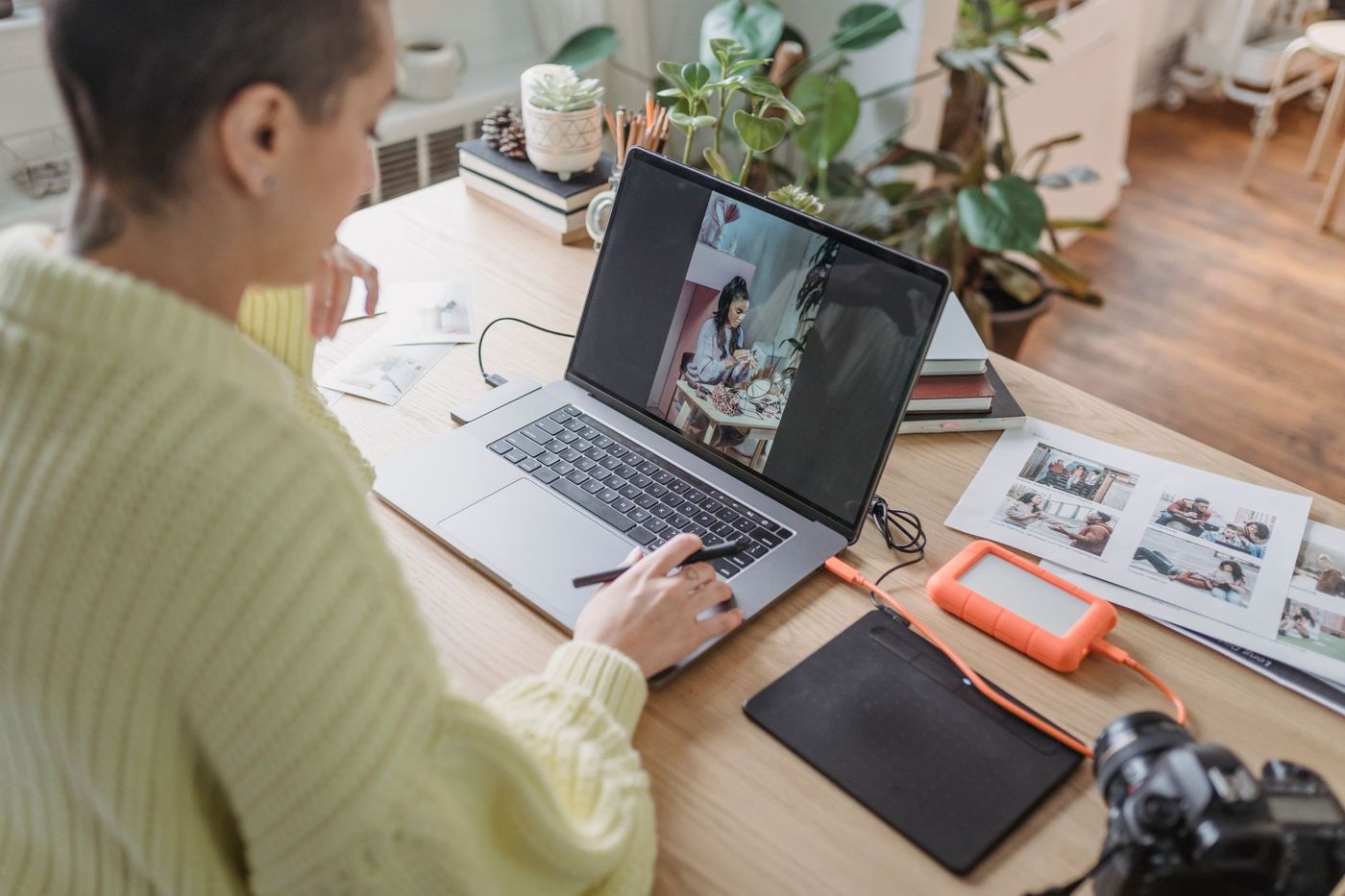 Vrouw bewerkt foto's op een laptop met een tekentablet, naast afdrukken, een externe schijf en een camera