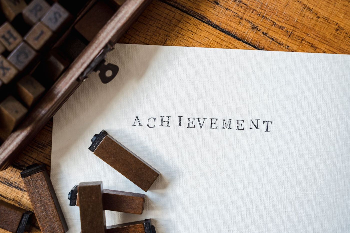 Houten letterstempels in een kistje naast een vel papier waarop met die stempels het woord ACHIEVEMENT is gestempeld