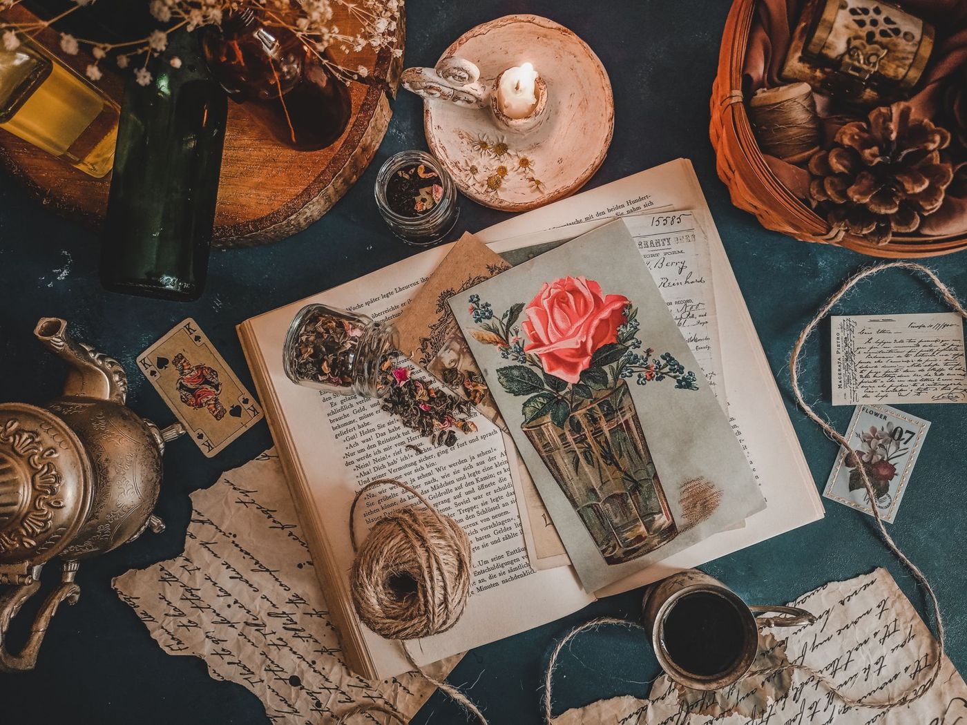 Bovenaanzicht van een oud boek met een ansichtkaart van een roos, handgeschreven briefjes, touw, kaars en theekopje